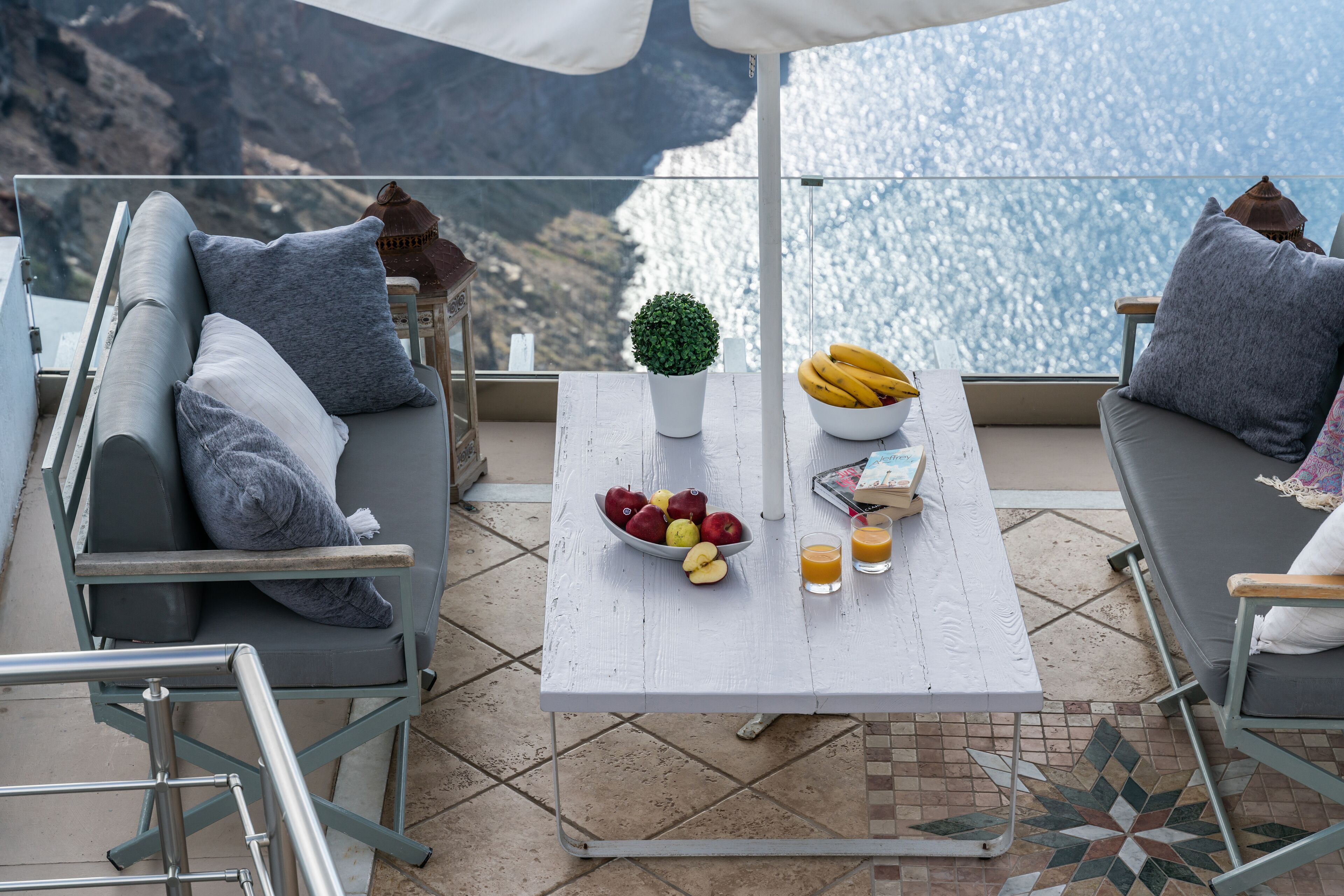 Una terraza con una mesa blanca, sofás grises, un frutero y una planta en maceta.