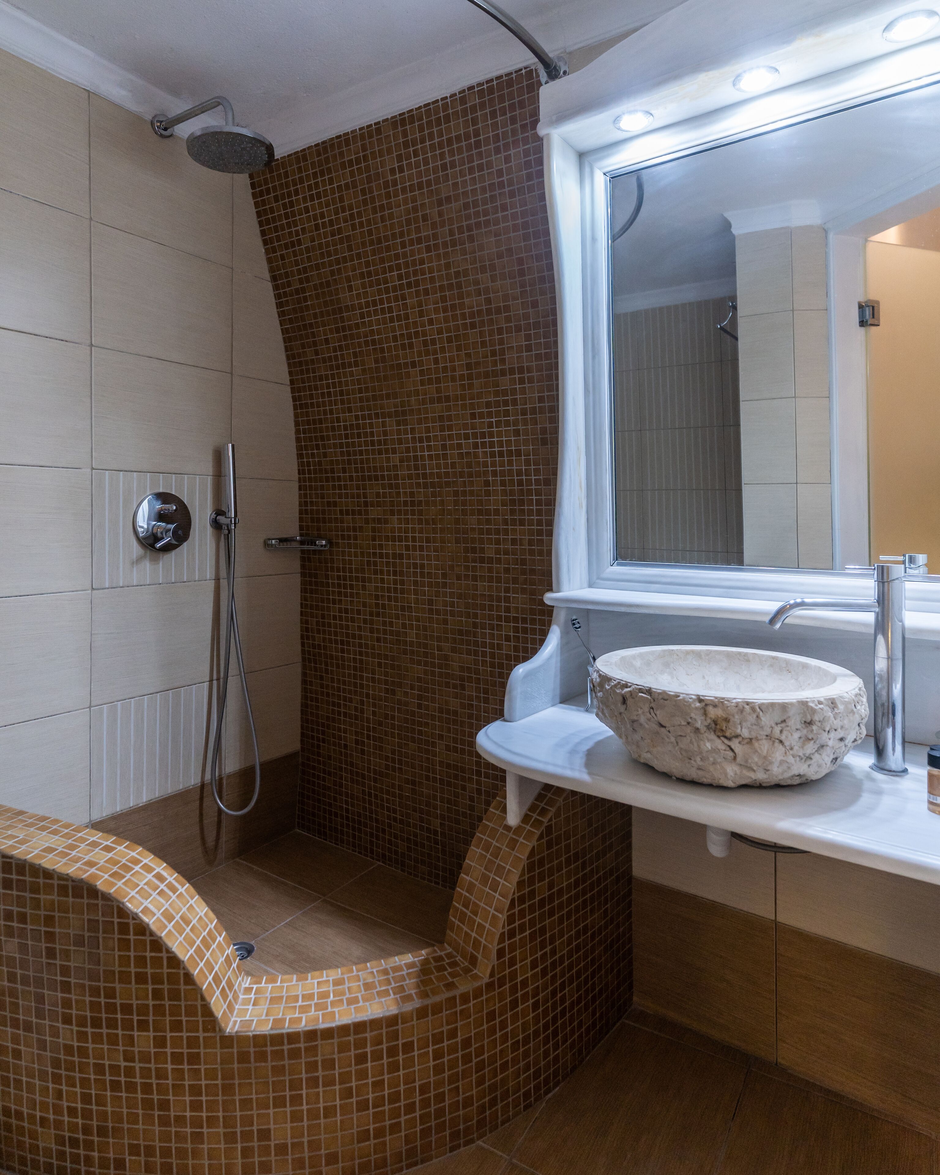 Un bagno con doccia, un lavabo con bacino in pietra e uno specchio sopra il lavabo.