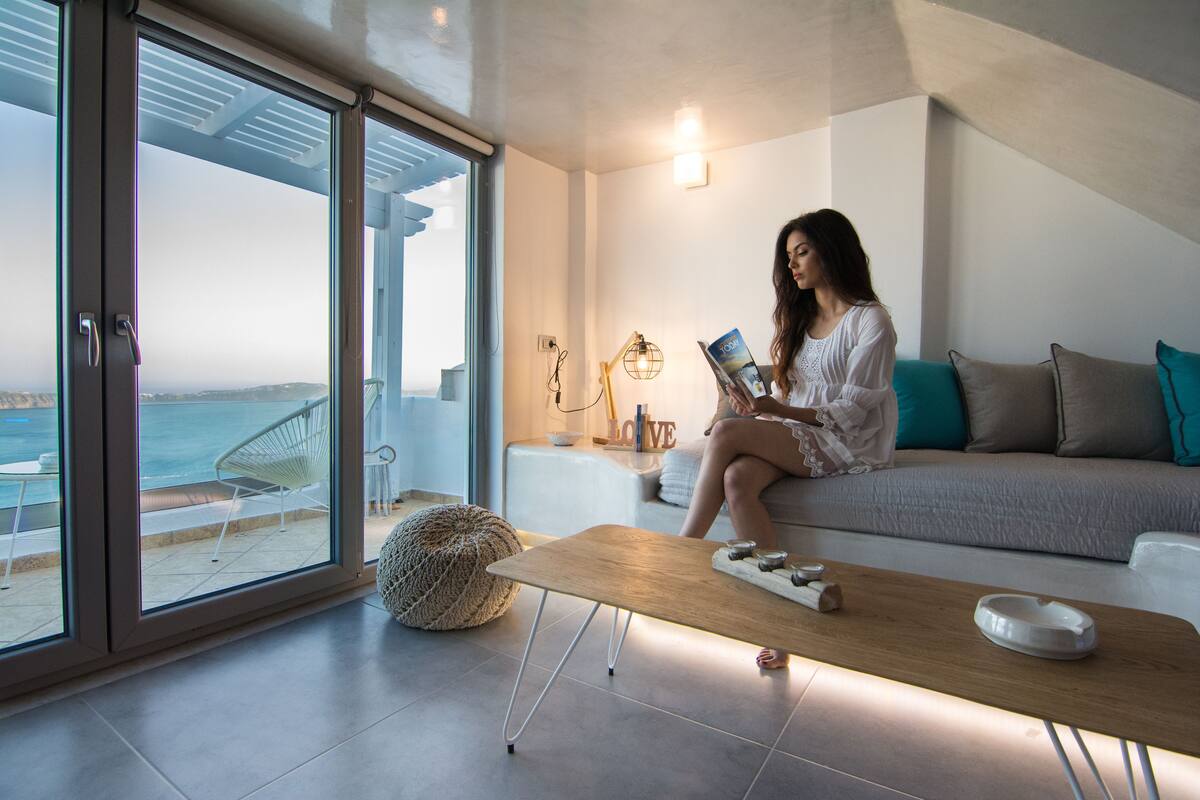 Una sala de estar moderna con un amplio ventanal que da a un balcón con vistas al mar.