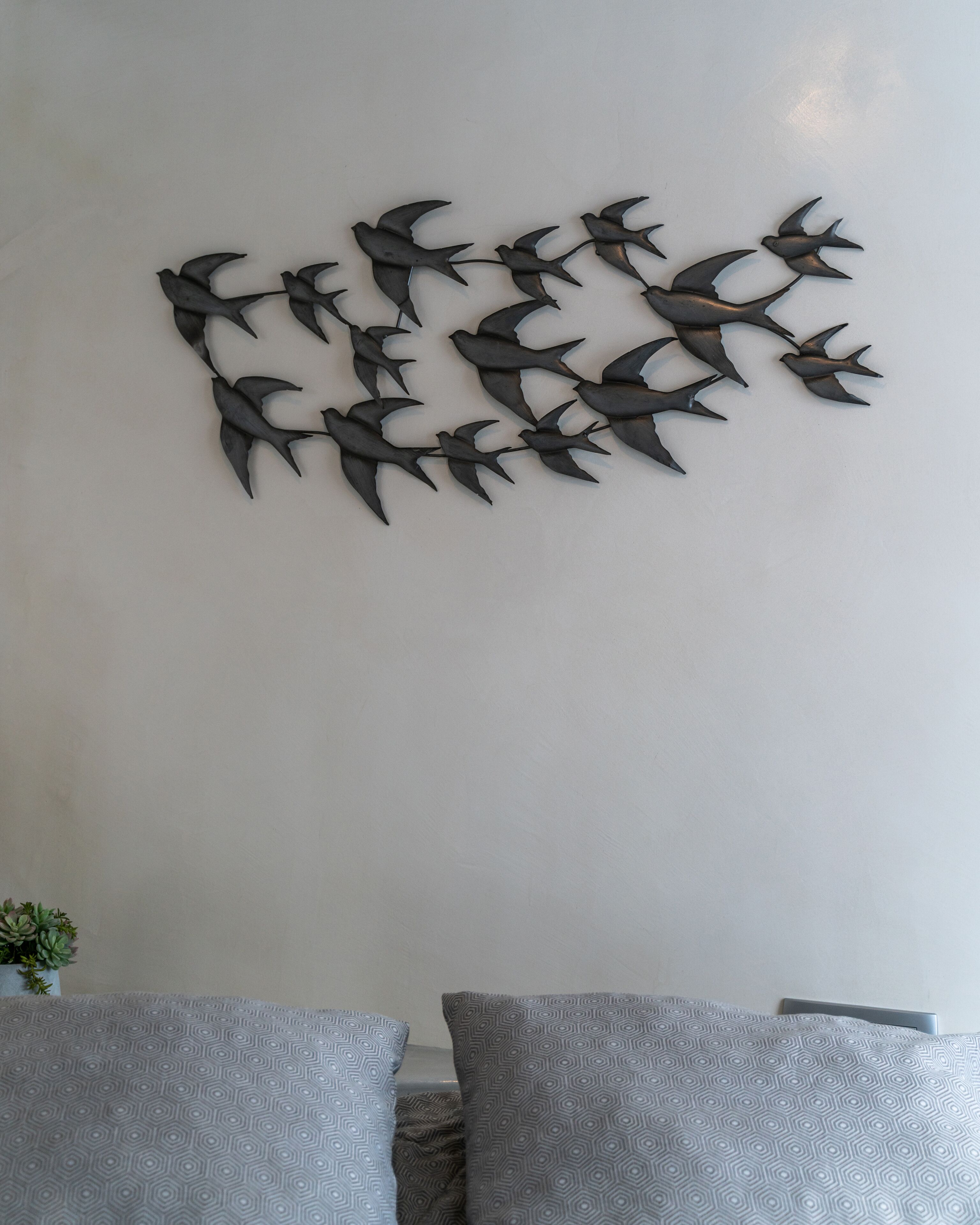 Una escultura metàl·lica penjada a la paret que representa ocells en vol.