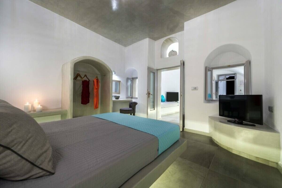 Un dormitorio moderno con cama, televisión y baño a la vista a través de un arco.