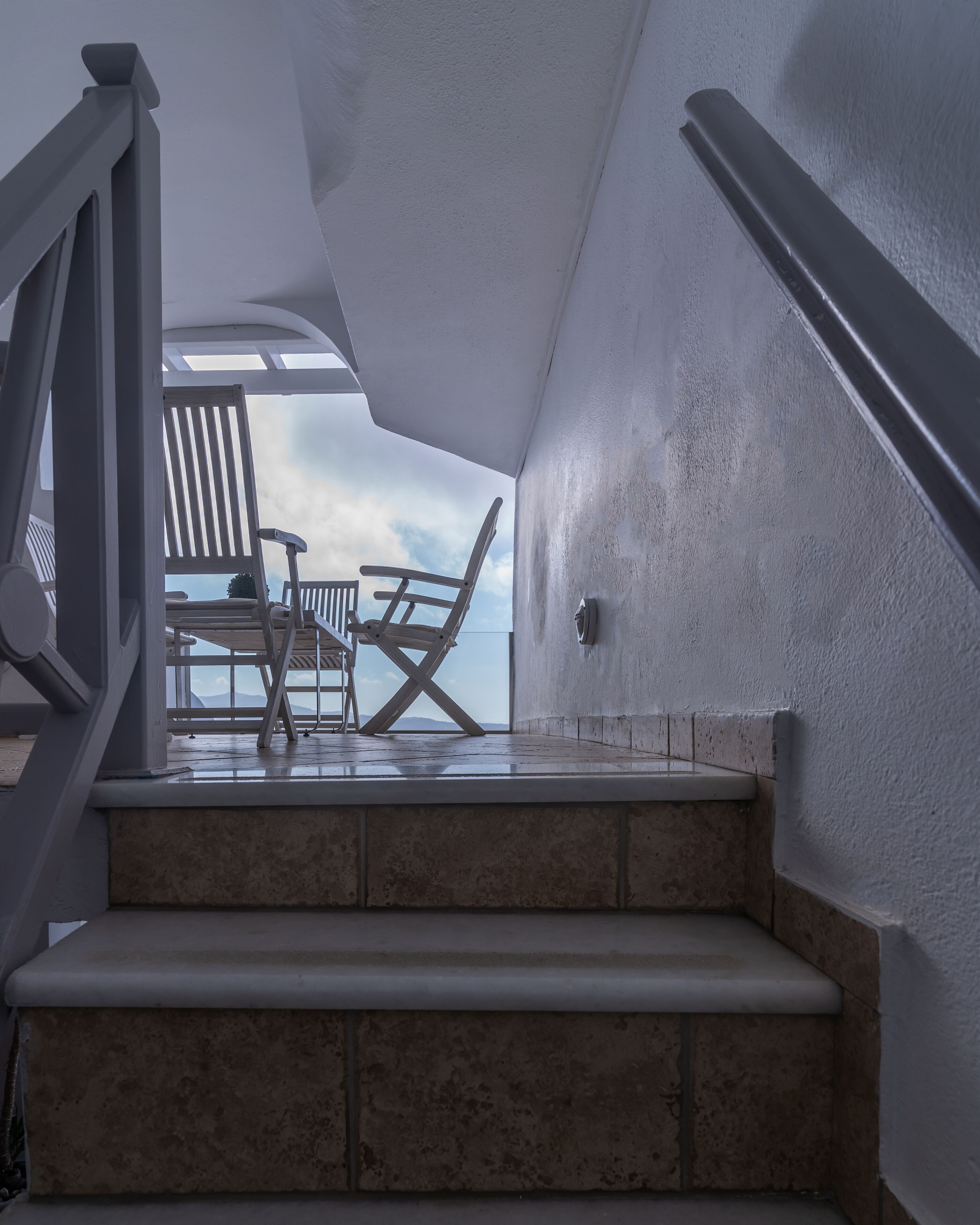 A set of outdoor stairs leading to a seating area with white chairs and a view of the sky.