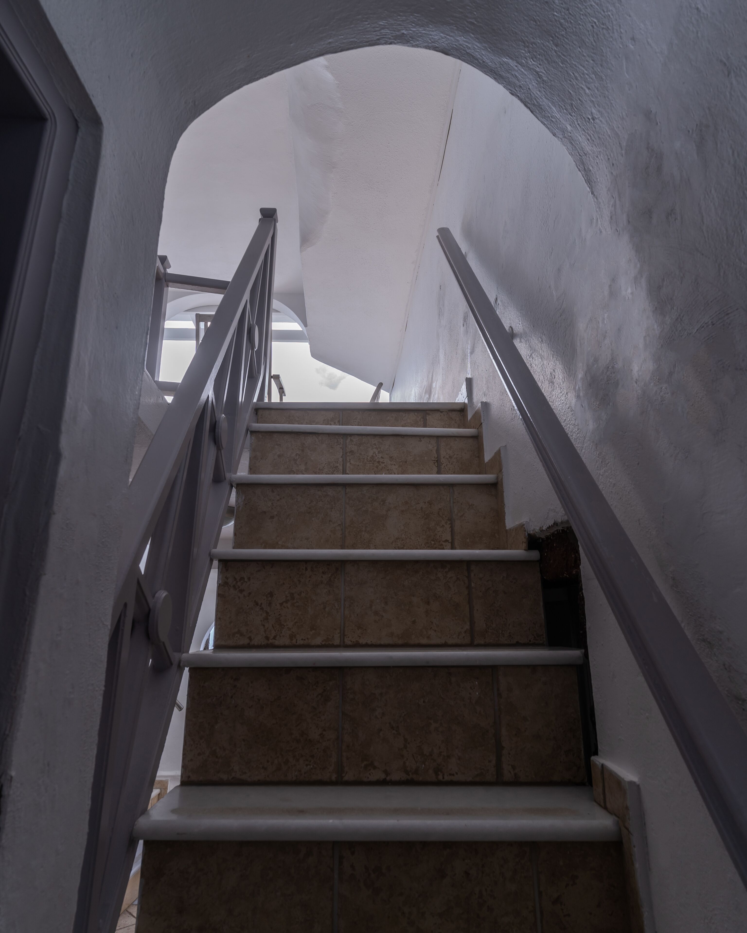 Una escalera con barandal blanco que lleva a una habitación con un ventanal grande.