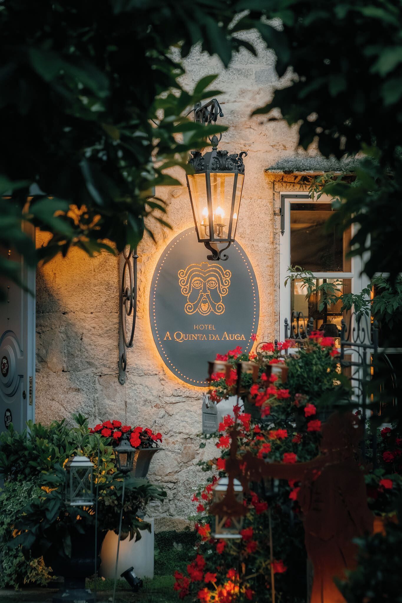 A stone wall with a circular sign for Hotel A Quinta da Augusta, surrounded by greenery and flowers.