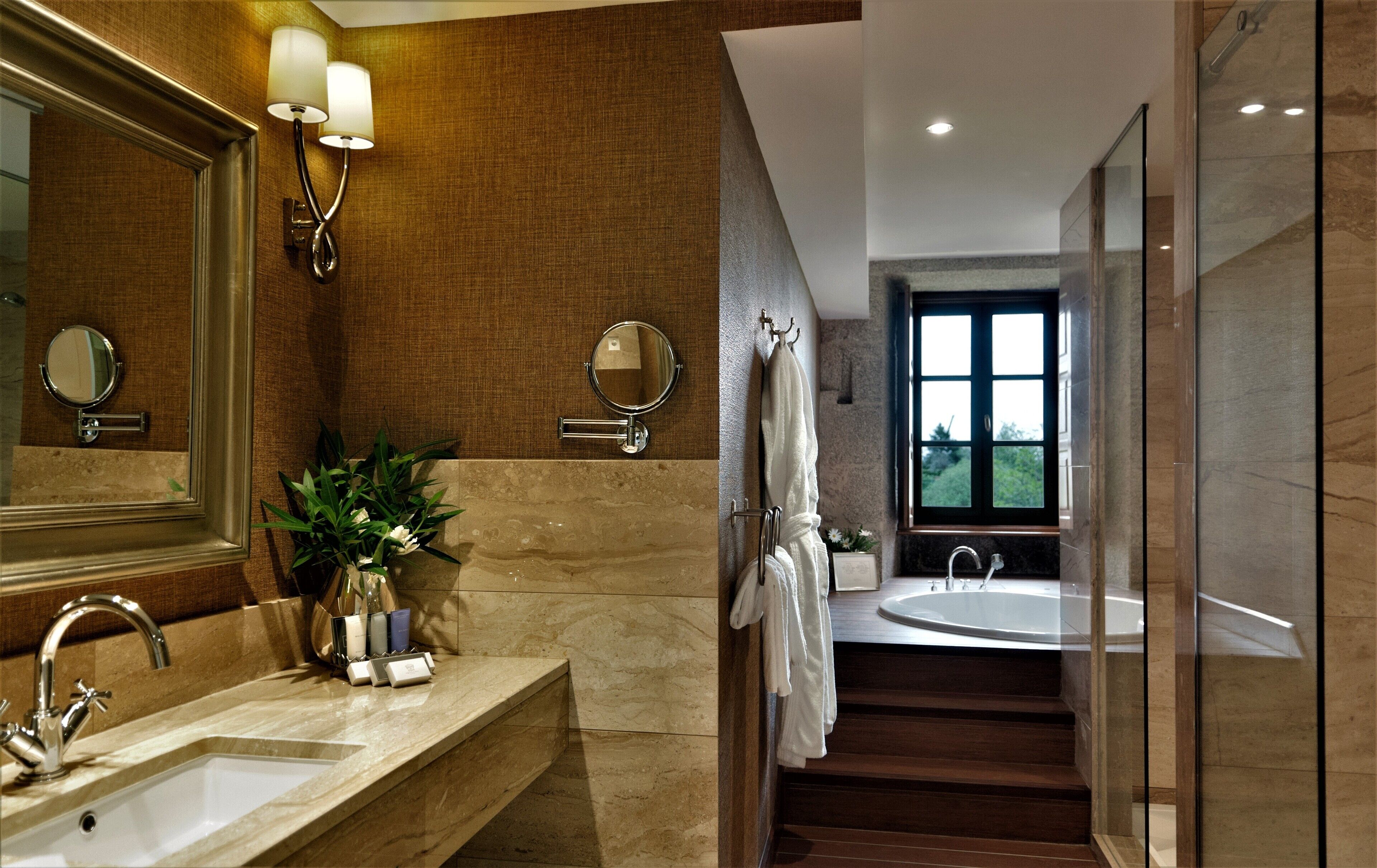 Un baño moderno con un espejo grande, dos luces empotradas, un lavamanos y una bañera.