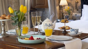 Une table en bois dressée pour le petit-déjeuner, avec des croissants, des fruits et un vase rempli de fleurs jaunes.