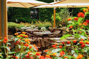 An outdoor dining area with tables and chairs, surrounded by greenery and flowers.