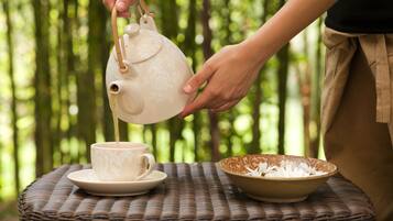 A person pouring tea from a teapot into a cup on a woven table.