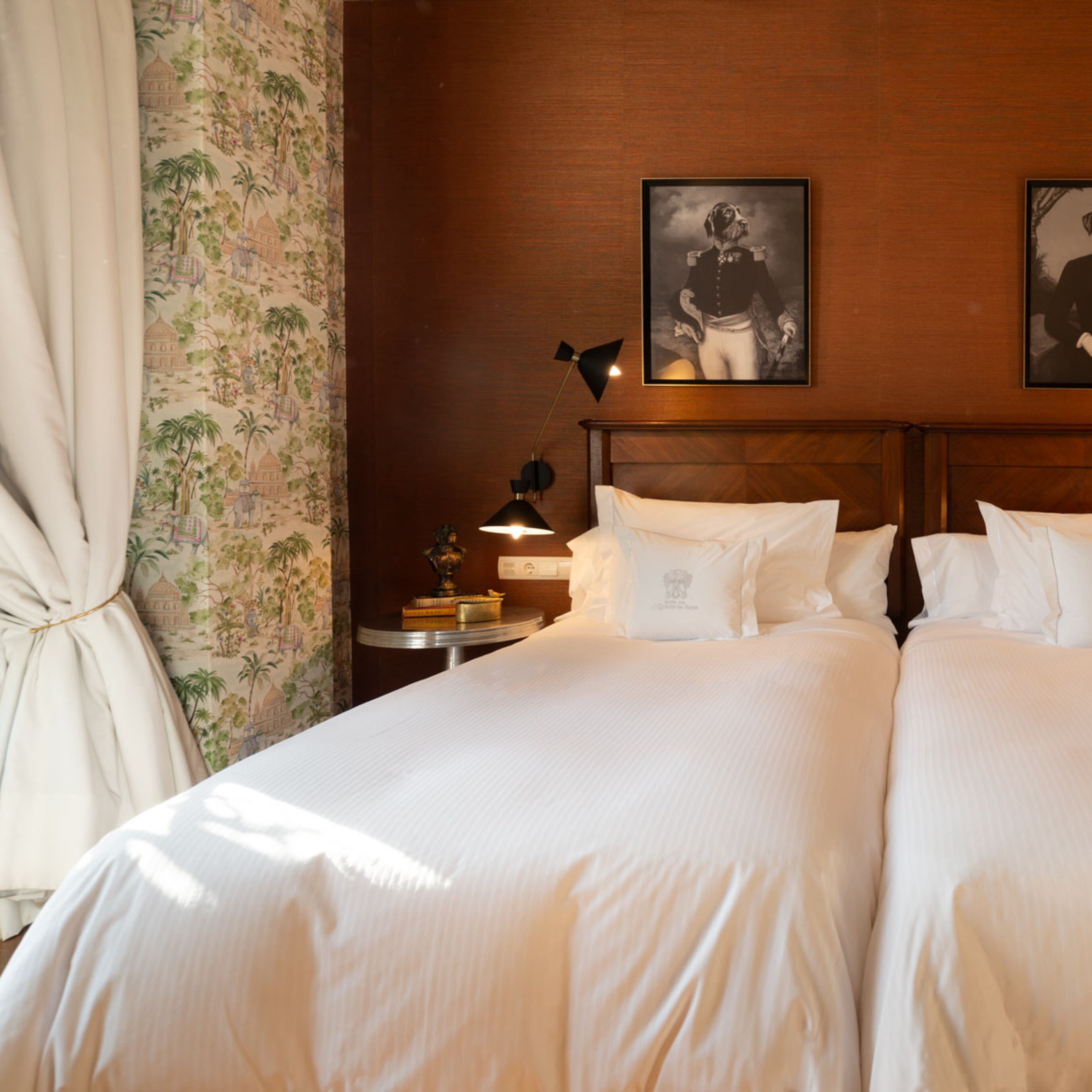 A hotel room with two beds, a nightstand with a lamp, and a wall-mounted picture.