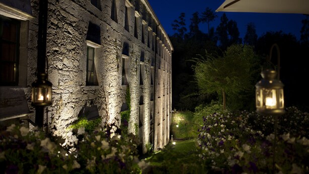 Un bâtiment en pierre doté de nombreuses fenêtres et un jardin agrémenté de fleurs et de lanternes.