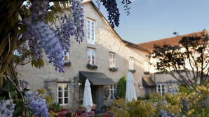 Un bâtiment en pierre avec un toit en pente, des fenêtres blanches et des parasols à l’extérieur.