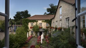 A courtyard with outdoor seating, a stone building, and a view through an open window.
