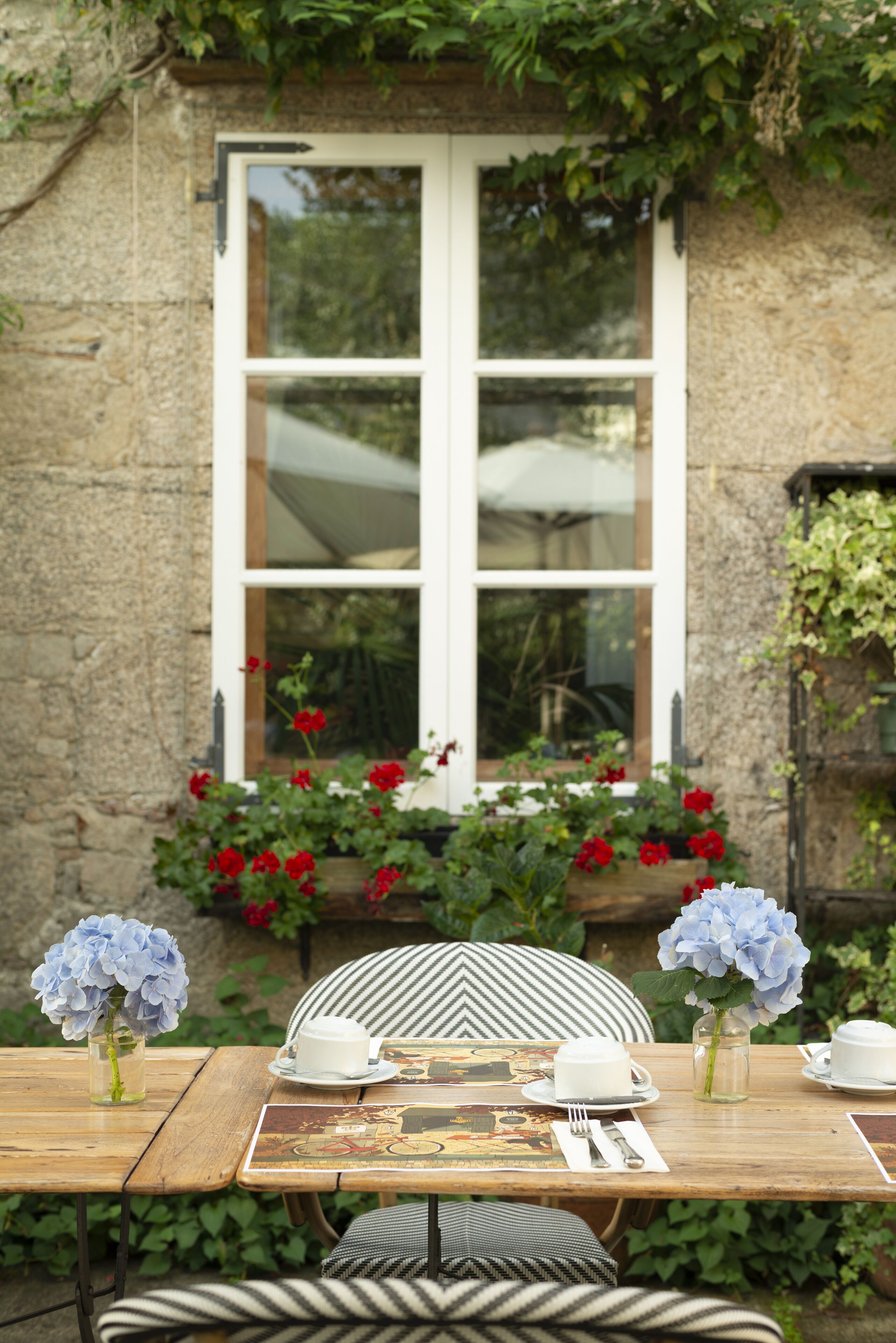 A wooden table set with white plates, silverware, and a vase of blue flowers.