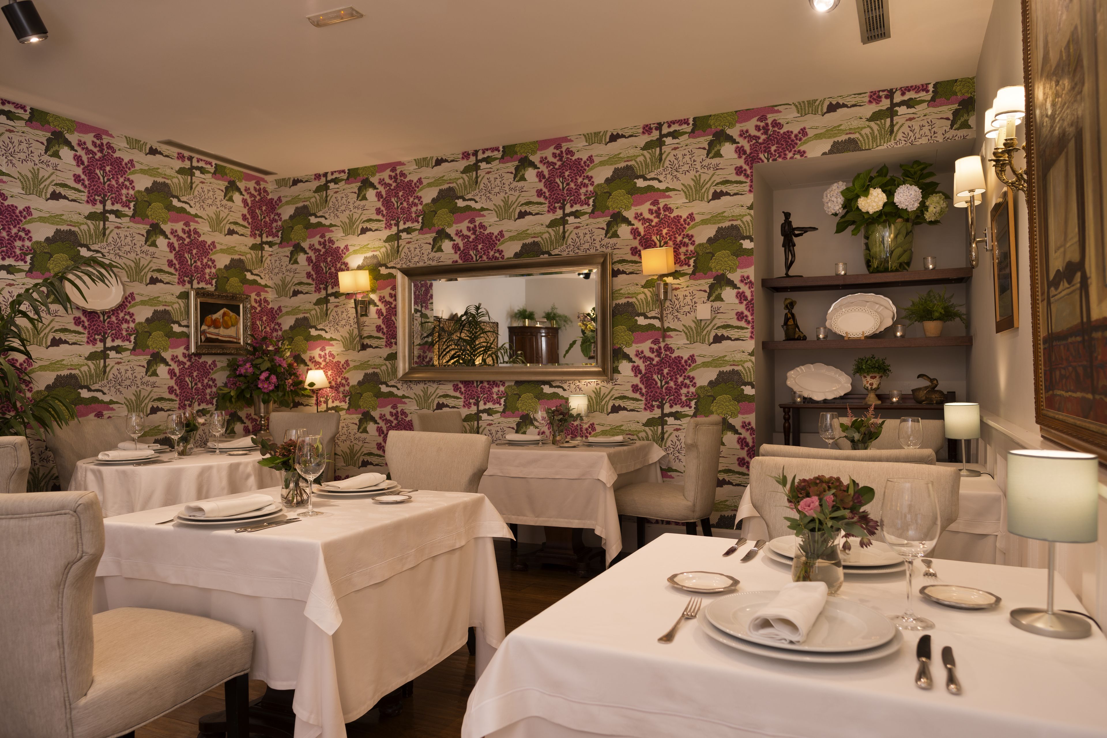 A dining area with tables set for a meal, surrounded by floral wallpaper and decorative lighting.