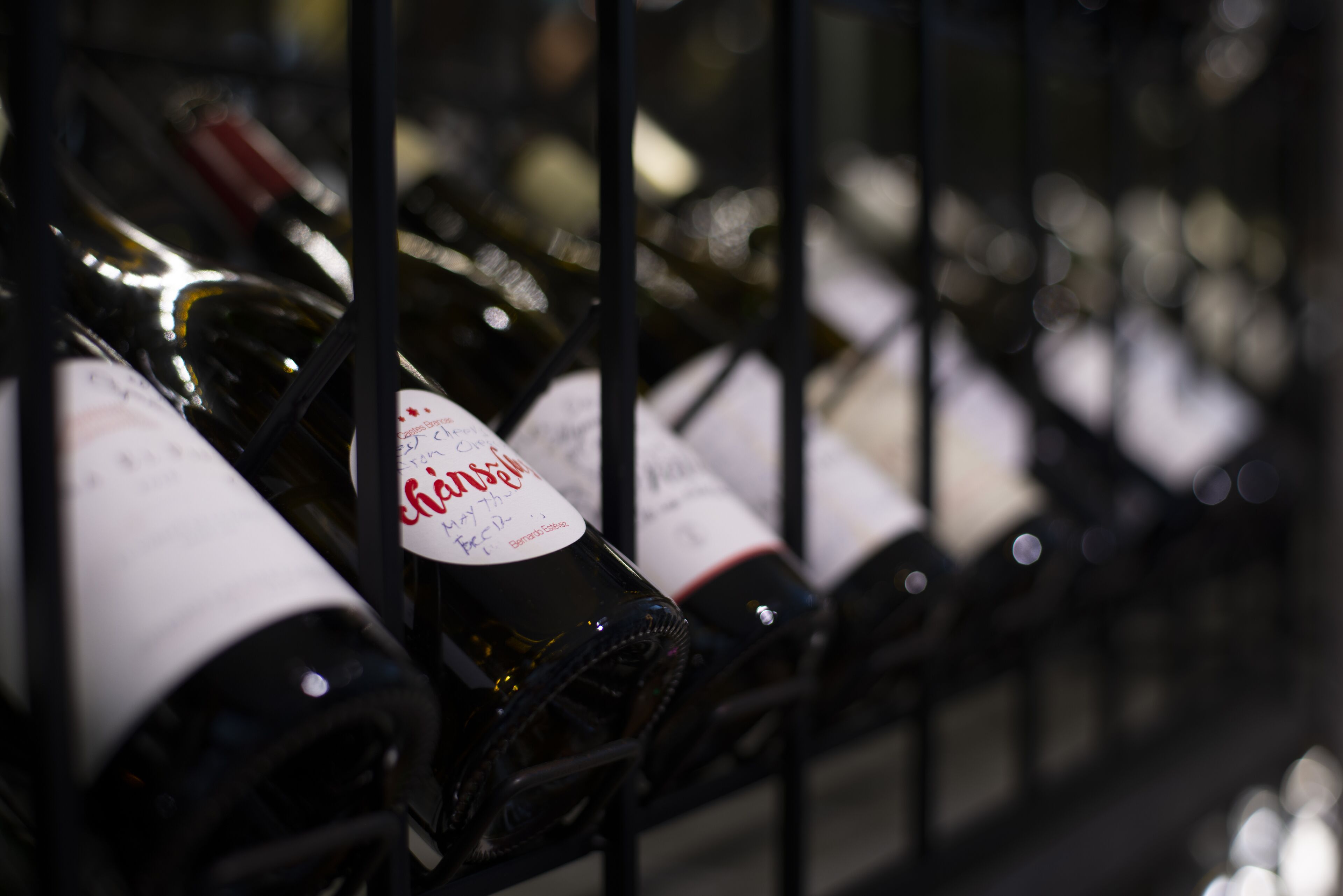 Una estantería con botellas de vino, algunas con etiquetas y notas escritas a mano.