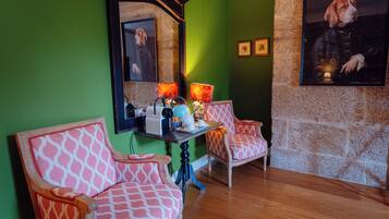 Una habitación con paredes verdes, suelo de madera, dos sillas estampadas, una mesa con una cafetera y un cuadro en la pared.
