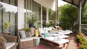 Un espace extérieur aménagé, abrité et doté de meubles en osier, de plantes en pot et d’un sol carrelé.