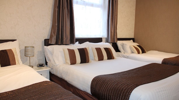 Une chambre d’hôtel avec trois lits, chacun doté de draps blancs et d’oreillers à rayures marron. On y trouve une table de chevet avec une lampe et un téléphone.