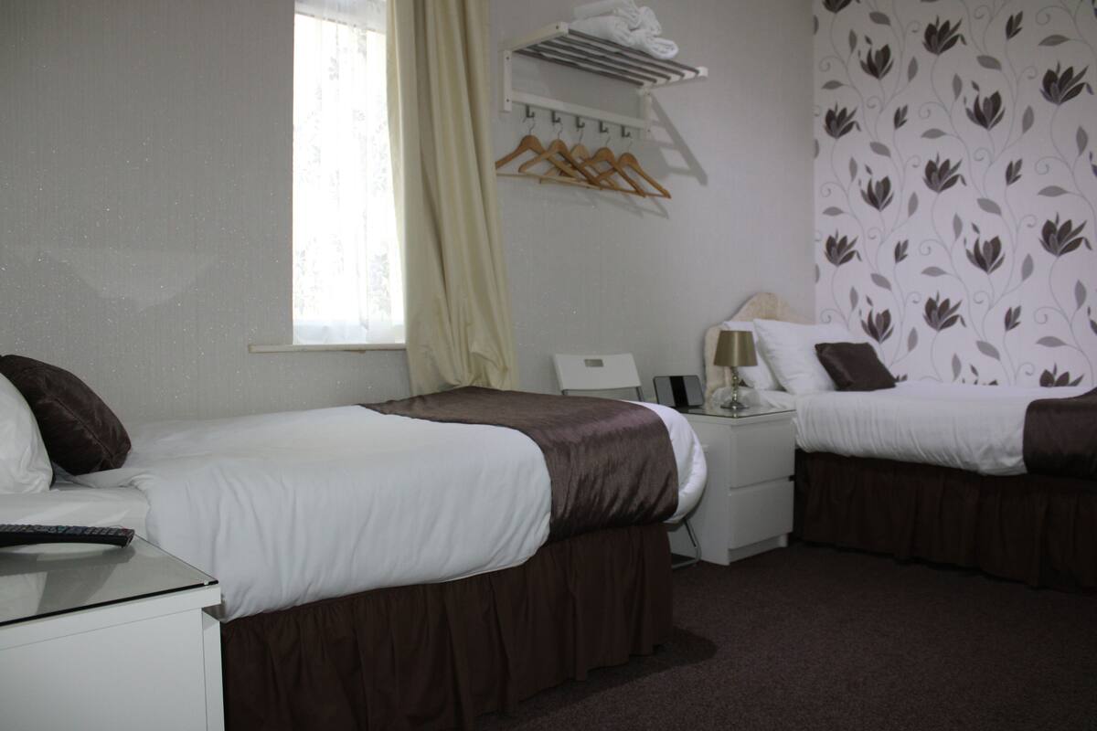 A hotel room with two beds, a desk, a chair, a lamp, and a window with curtains.