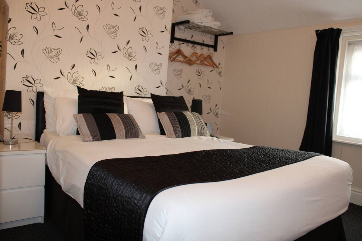 A neatly made bed with a black and white bedspread, a bedside table with a lamp, and a wall-mounted shelf with towels.