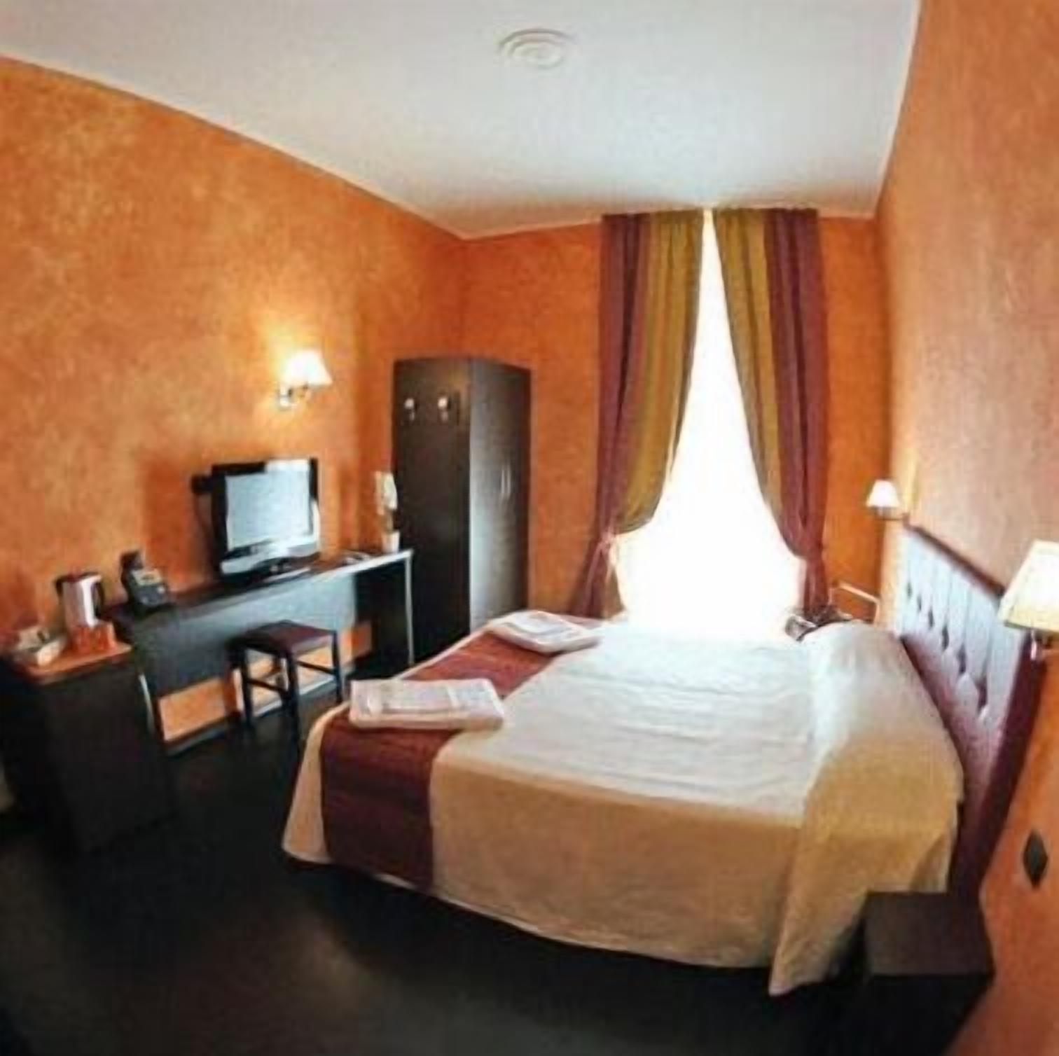 A hotel room with a bed, a desk, a television, and a wardrobe.