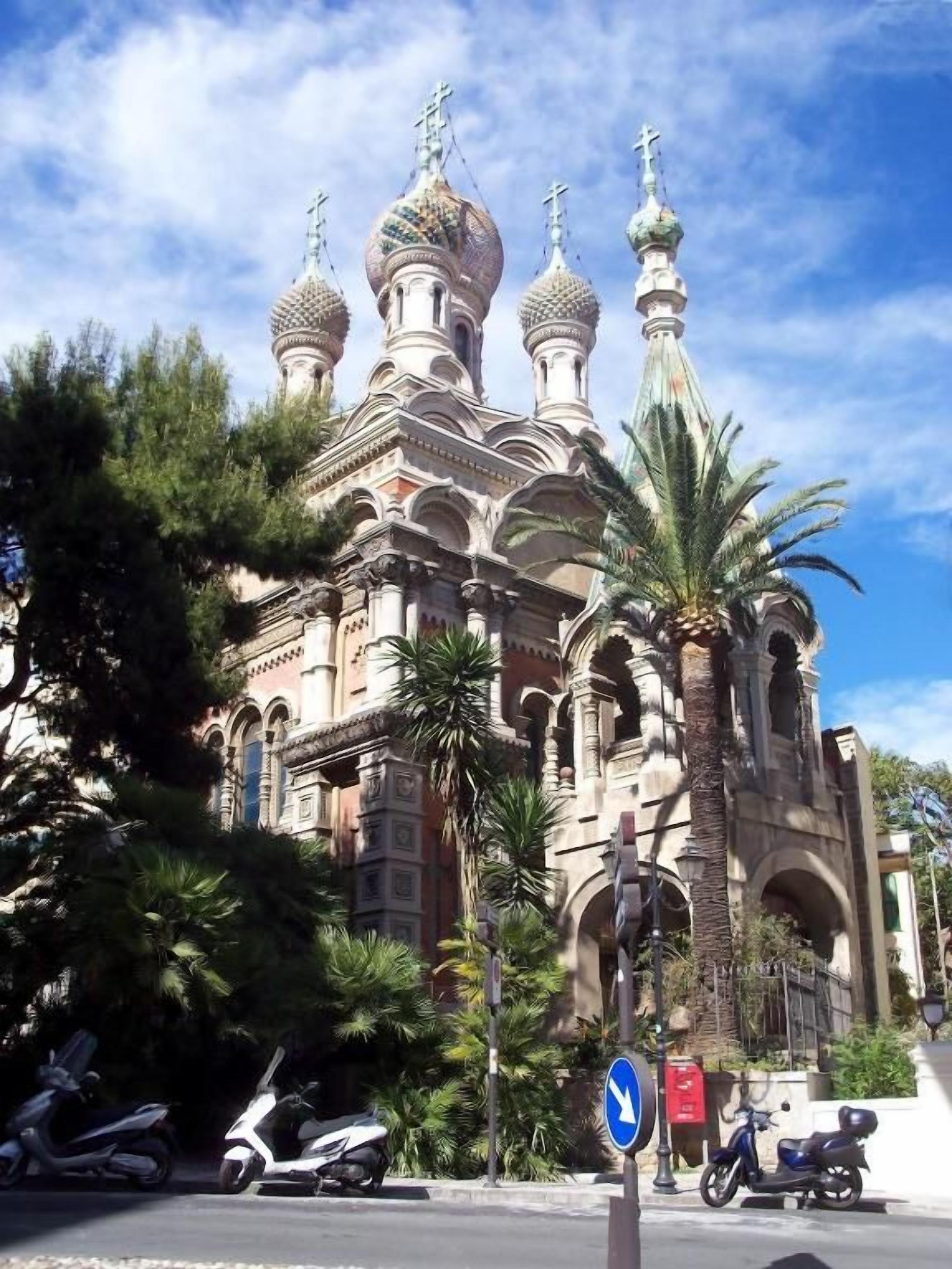Un edificio con múltiples cúpulas y cruces, rodeado de palmeras y scooters estacionados.