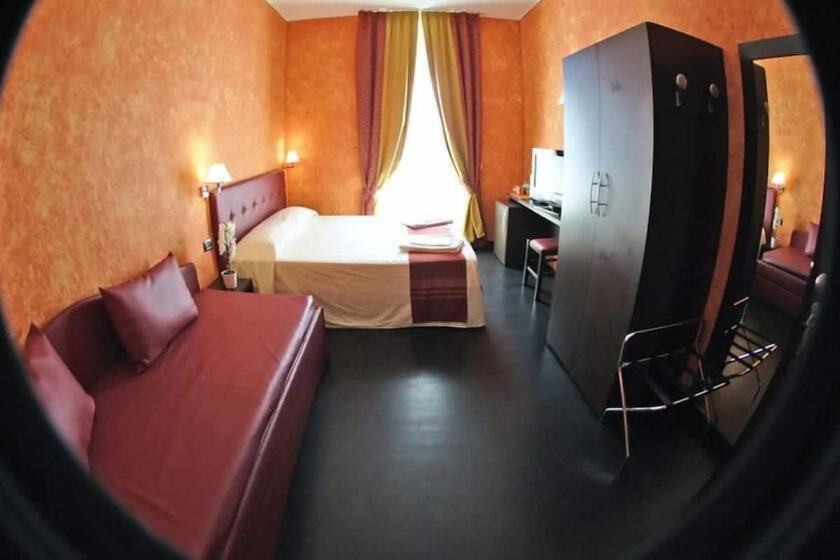 A compact hotel room with a bed, a desk, and a wardrobe.