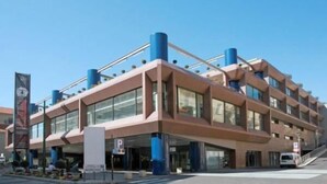 Un edificio moderno con un diseño arquitectónico único, que destaca por sus amplios ventanales y una llamativa combinación de colores azul y beige.