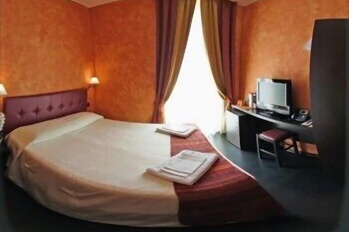 A hotel room with a bed, a desk with a computer, and a TV.