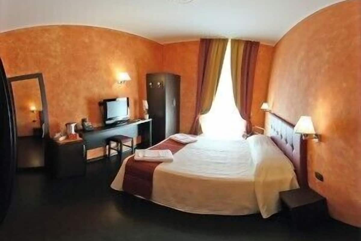 A hotel room with a bed, a desk, a chair, a wardrobe, and a television.