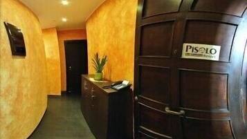 A reception area with a wooden reception desk, a potted plant, and a door labeled "PISOLO."