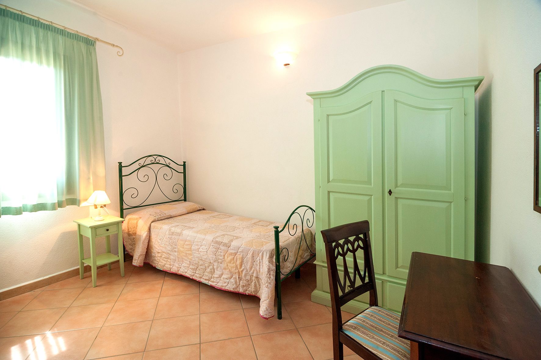 A bedroom with a bed, a nightstand, a chair, a wardrobe, and a window with curtains.
