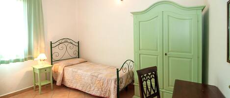 A bedroom with a bed, a nightstand, a chair, a wardrobe, and a window with curtains.