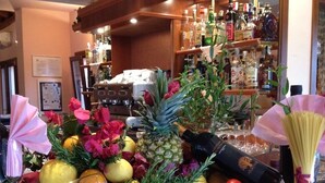 Una zona de bar con una variedad de botellas y vasos, una barra de madera y una exhibición de frutas y flores.