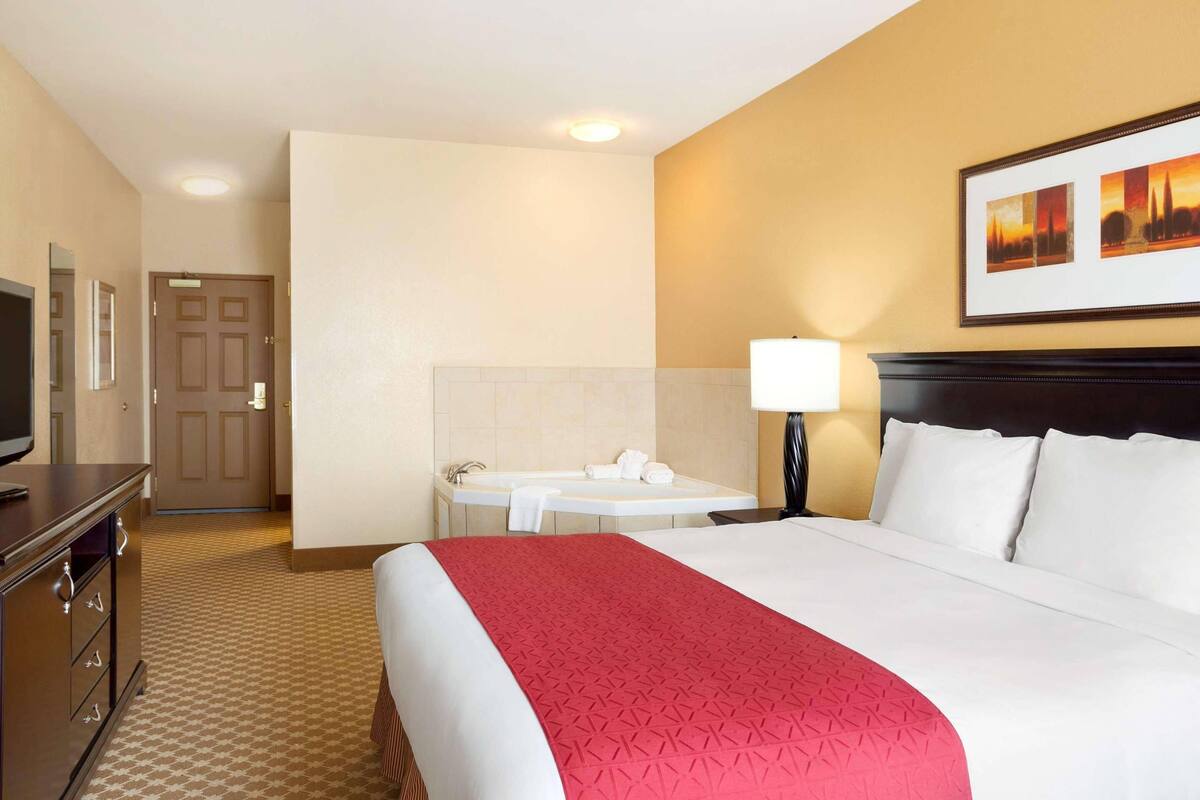 Une chambre d’hôtel avec un grand lit, un bureau avec une lampe, une salle de bain avec une baignoire et un téléviseur posé sur une commode.