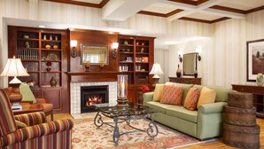 A well-furnished living room with a fireplace, a green sofa, striped armchairs, a glass coffee table, and a bookshelf. - Country Inn & Suites by Radisson, Conway, AR (Conway)