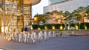 A modern building with a glass facade and a seating area with chairs arranged for an event.