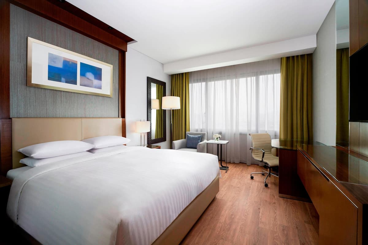 A hotel room with a large bed, a desk, a chair, a TV, and a window with curtains.