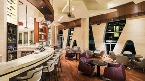 A modern bar area with a curved counter, bar stools, and a seating area with leather chairs and tables.