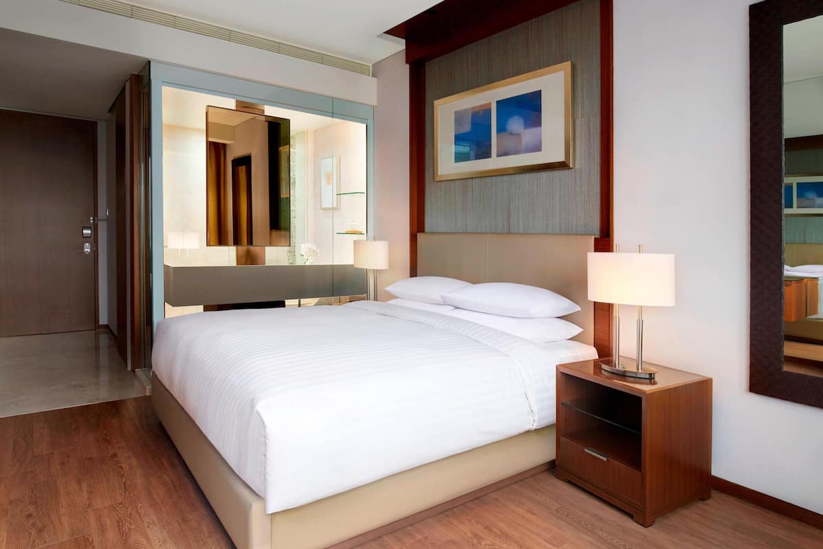 A hotel room with a large bed, a bedside table with a lamp, a mirror, and a framed picture on the wall.
