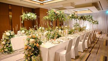 A banquet hall with long tables set for a formal event, adorned with floral arrangements and candles.