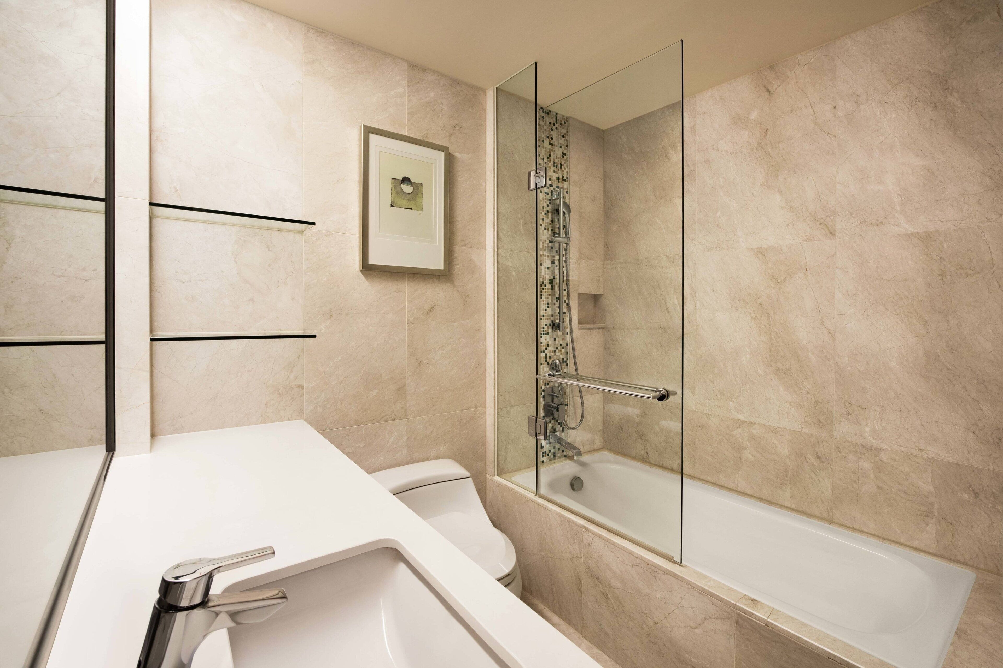 Une salle de bain moderne avec un lavabo blanc, des toilettes et une douche séparée par une paroi de verre.