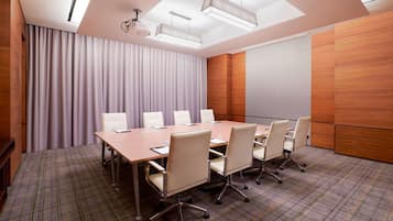 A conference room with a long table, six chairs, a projector, and a large screen.