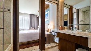 A hotel room with a large bed, a bathroom with a mirror, and a shower area.