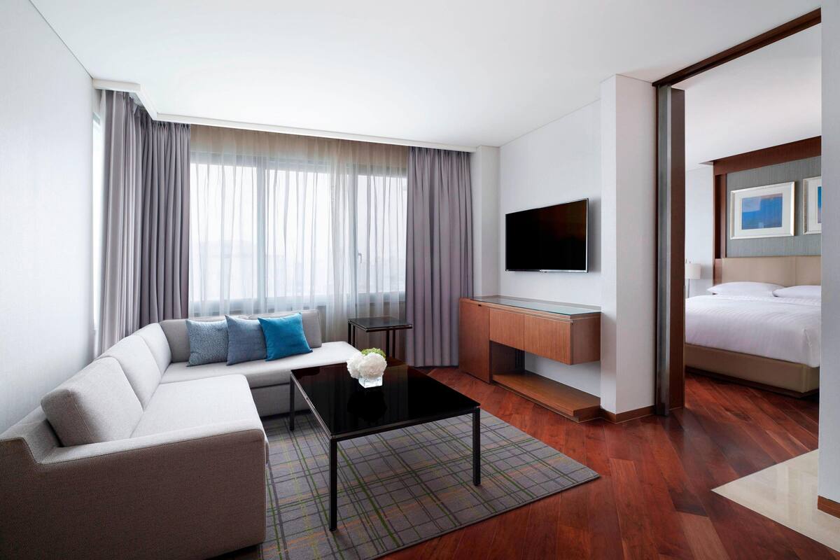 A modern hotel room with a sofa, a coffee table, a TV, a desk, and a bed.