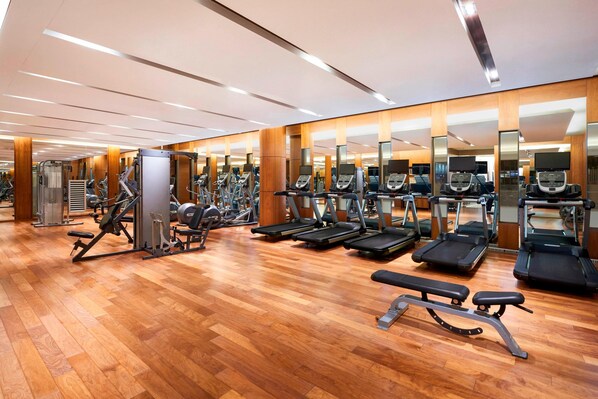Une salle de sport spacieuse équipée de plusieurs tapis de course, de machines de musculation et de bancs.