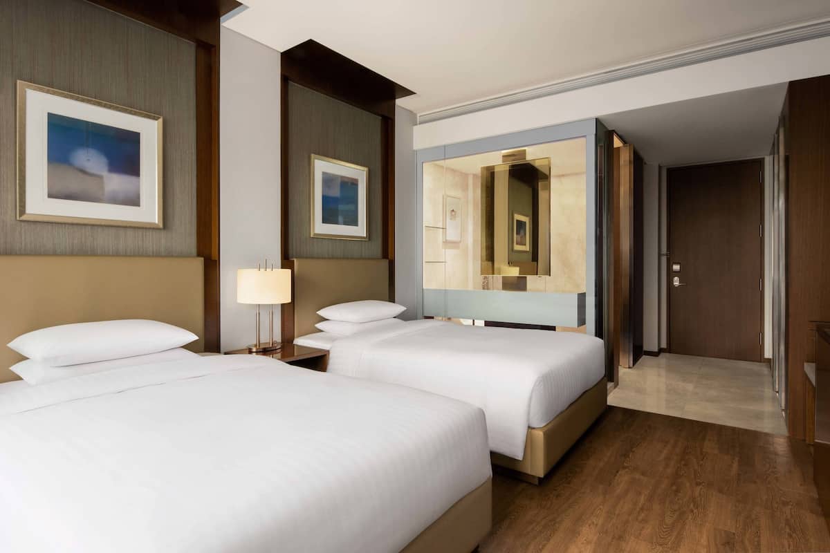A hotel room with two beds, a large mirror, and a wooden floor.