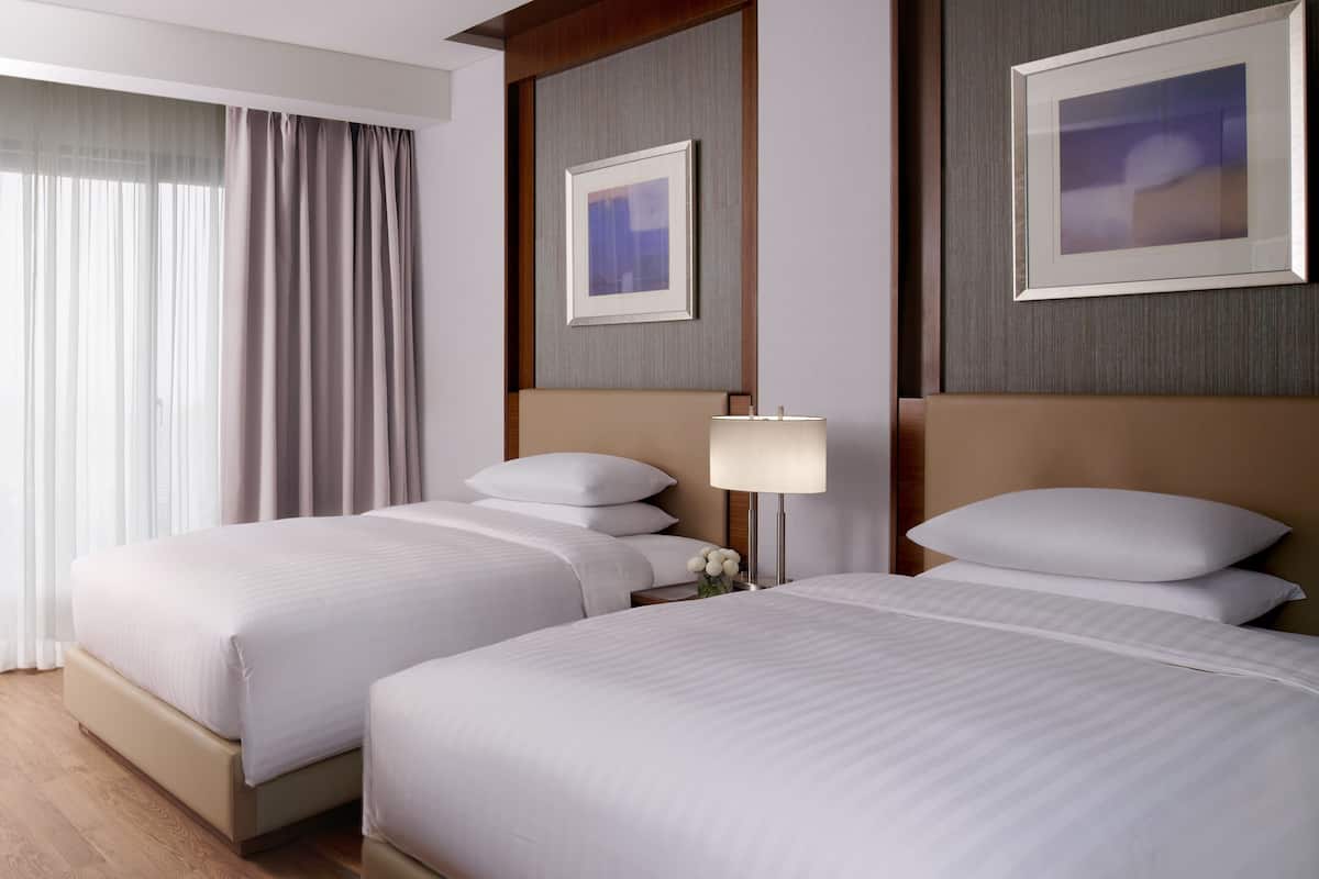 A hotel room with two beds, a nightstand, a lamp, and framed artwork on the walls.