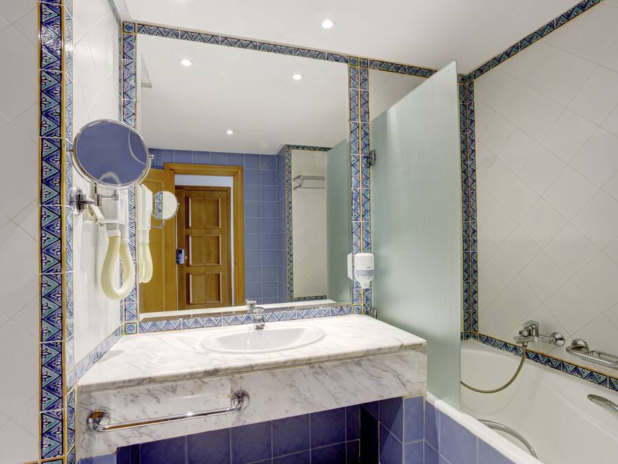Un baño con lavamanos de mármol, espejo de mano y bañera con ducha.