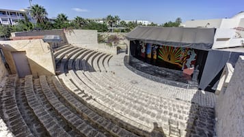 Een openluchttheater met terrasvormige stenen zitplaatsen en een podium met kleurrijke achtergronddecoraties.